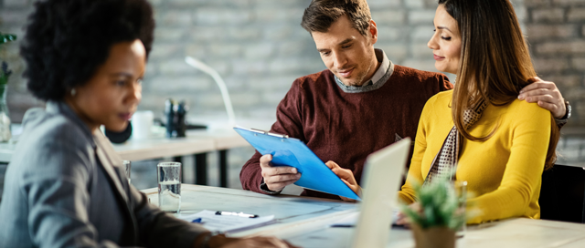 A financial advisor meets with a young couple reviewing documents together.